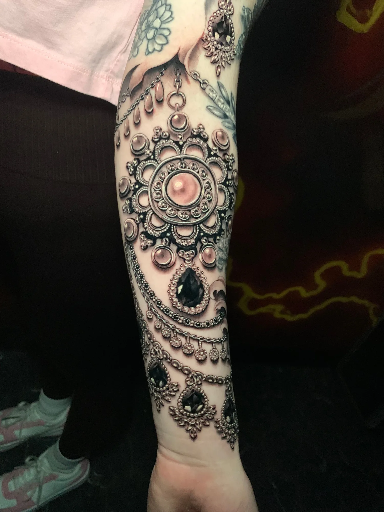 Hyper realistic jewelry tattoo done in black and grey on the forearm.