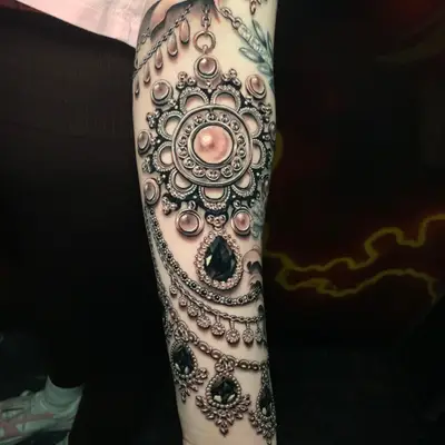 Hyper realistic jewelry tattoo done in black and grey on the forearm.