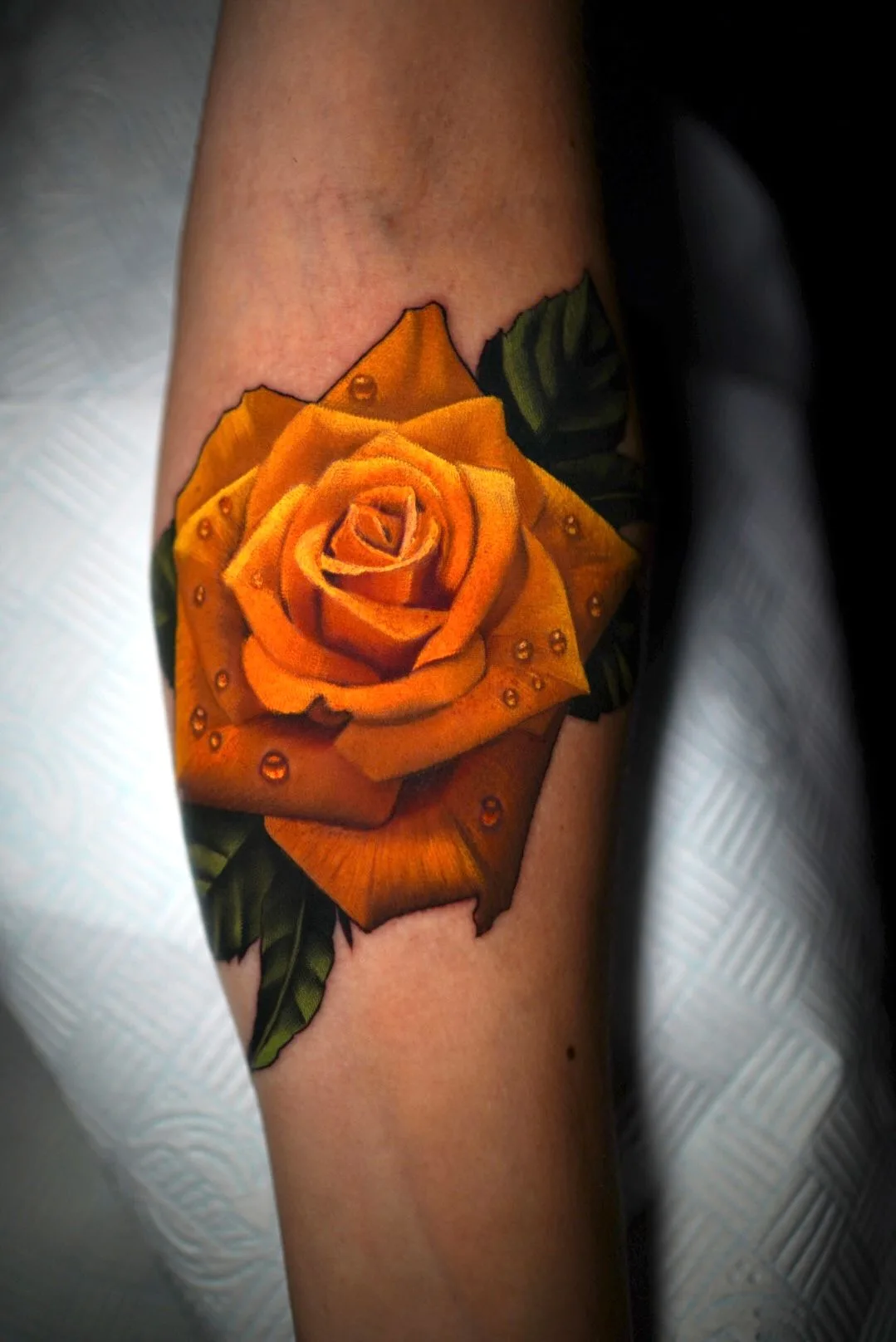 Tattoo of a yellow rose with water droplets in a reaslim style.