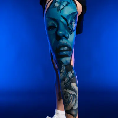 Tattoo of a blue face with butterflies on a leg
