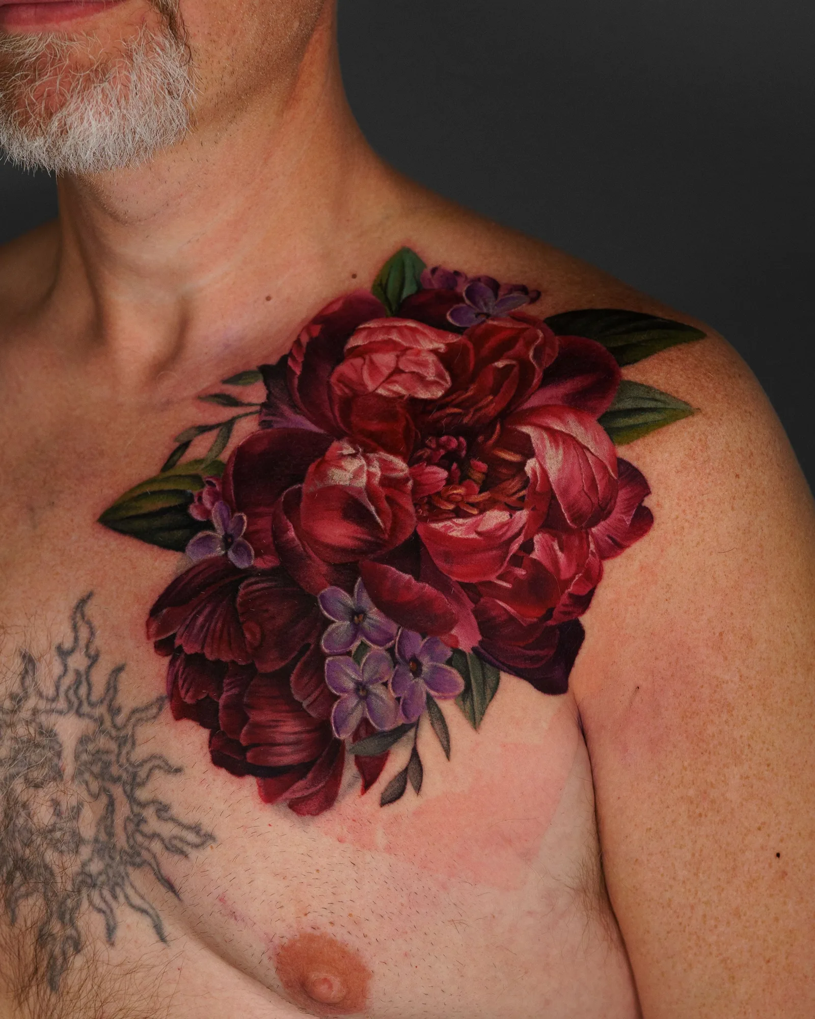 A vibrant floral tattoo covering the shoulder and upper chest area, featuring red peonies and purple flowers.