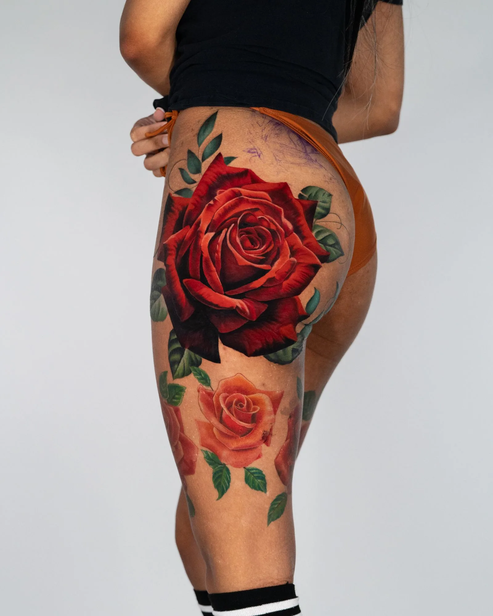 Vibrant floral tattoo featuring red and orange roses on a hip/butt.