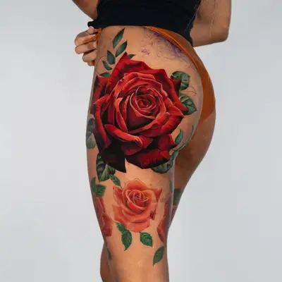 Vibrant floral tattoo featuring red and orange roses on a hip/butt.