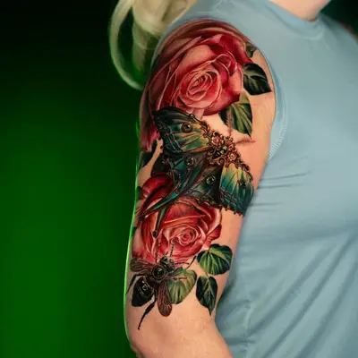 A vibrant tattoo featuring roses and gilded insects on an upper arm.