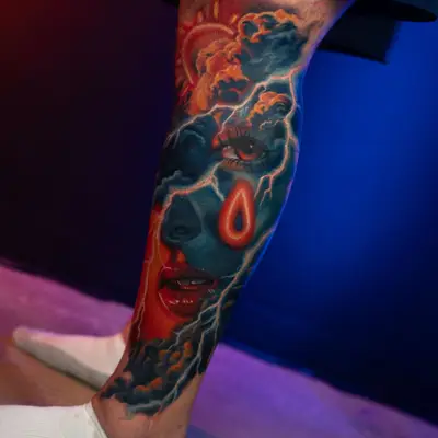 A vibrant leg tattoo featuring a face, raindrops, and storm clouds in vivid colors with an orange and blue neon palette.