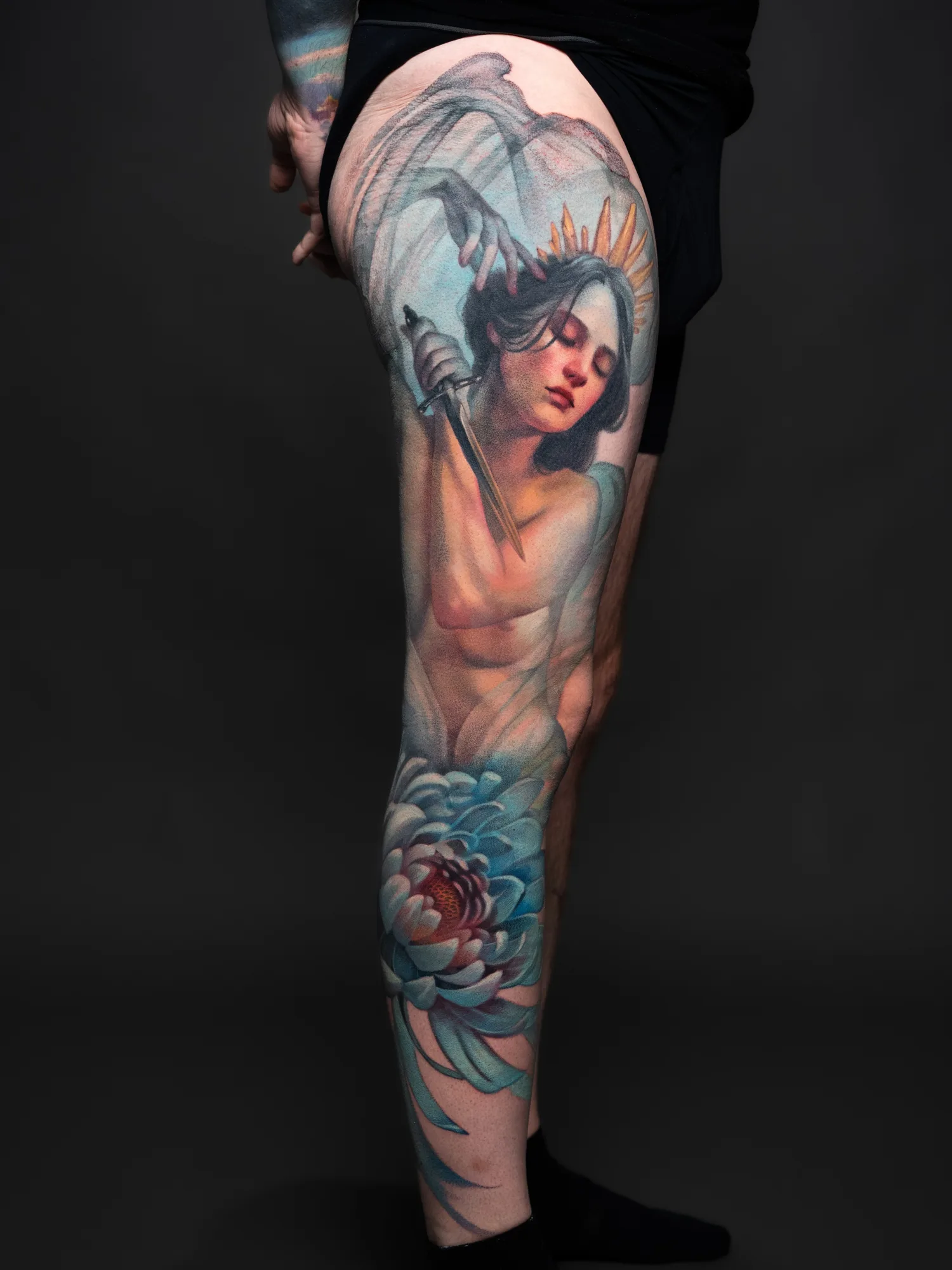 Leg tattoo of an angel with a sword and a large blue flower.