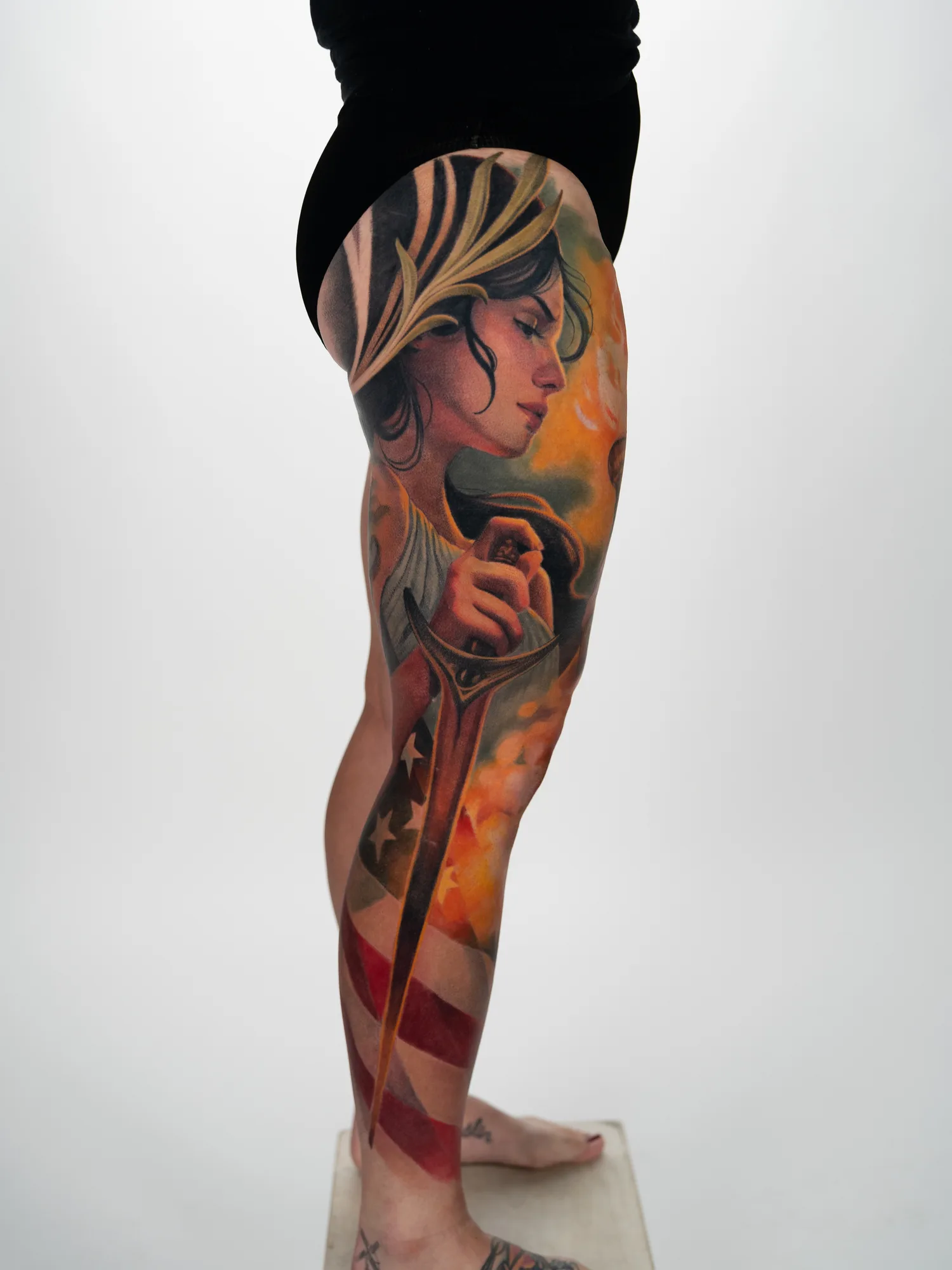 A leg tattoo featuring a woman with a sword and an American flag, showcasing vivid colors.