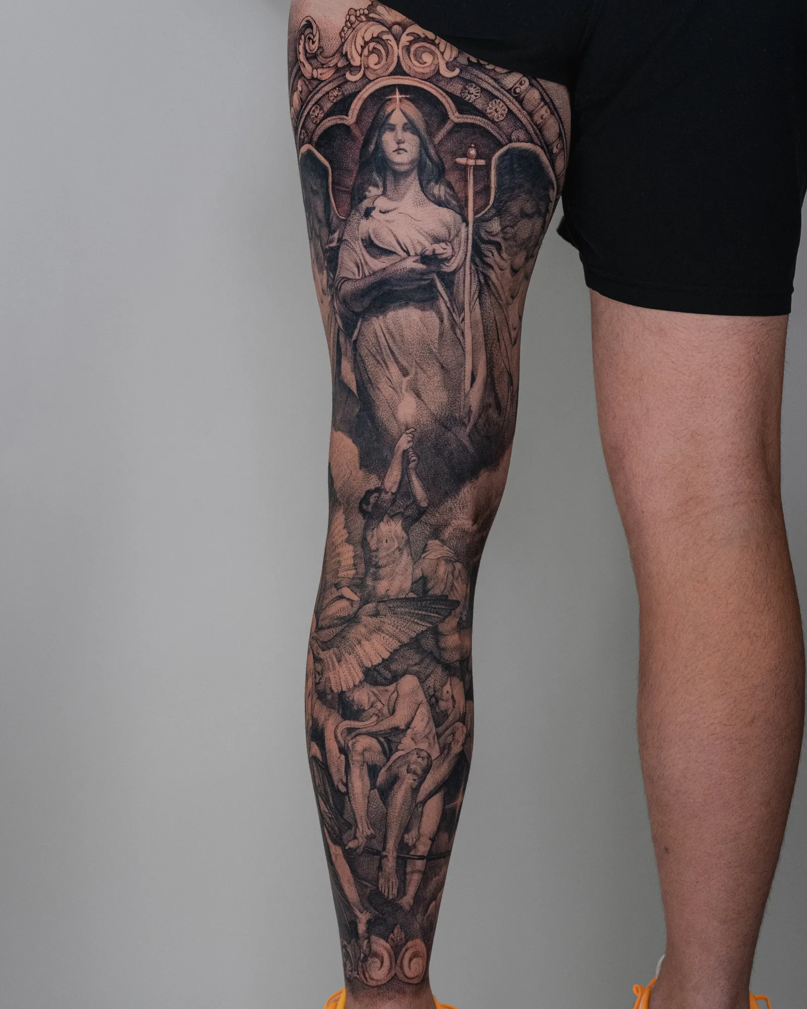 Full leg tattoo with angels and figures in black and grey.