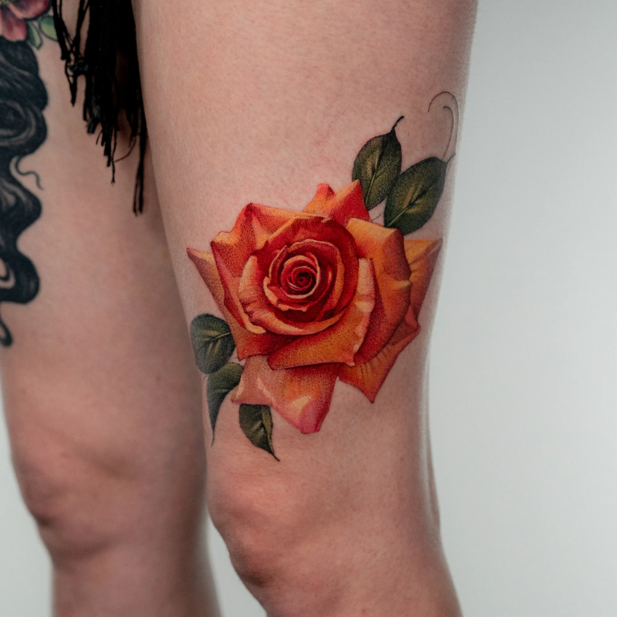 Orange rose in a realism style on a thigh.