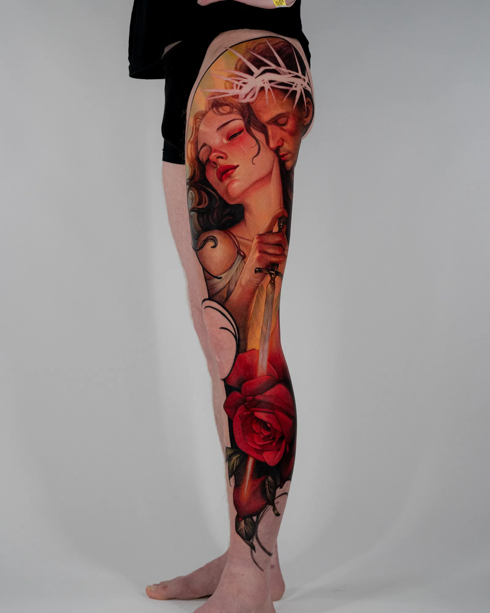Leg sleeve tattoo of two figures with a red rose in a painterly realism style.
