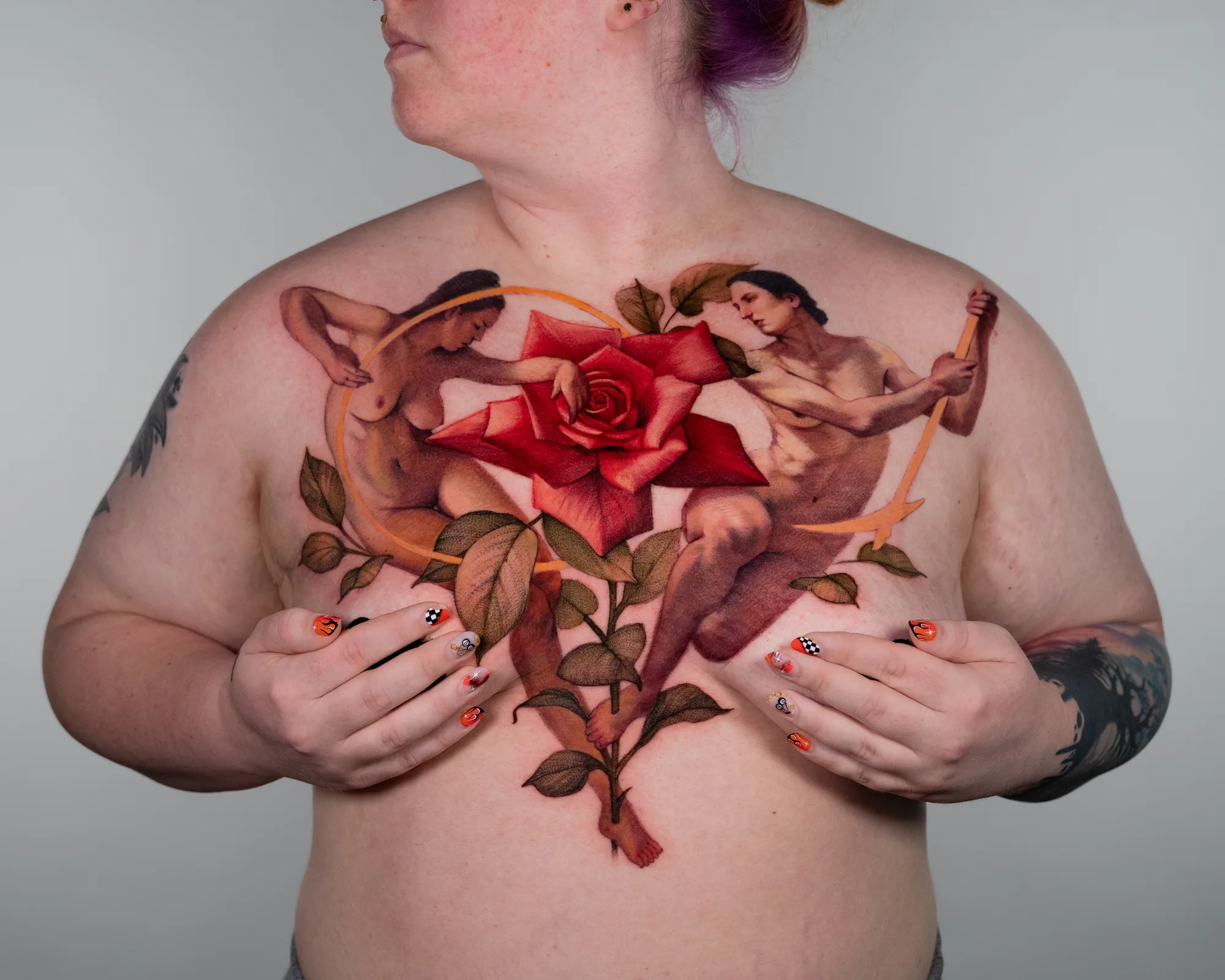 Chest tattoo with a rose and two nude figures.