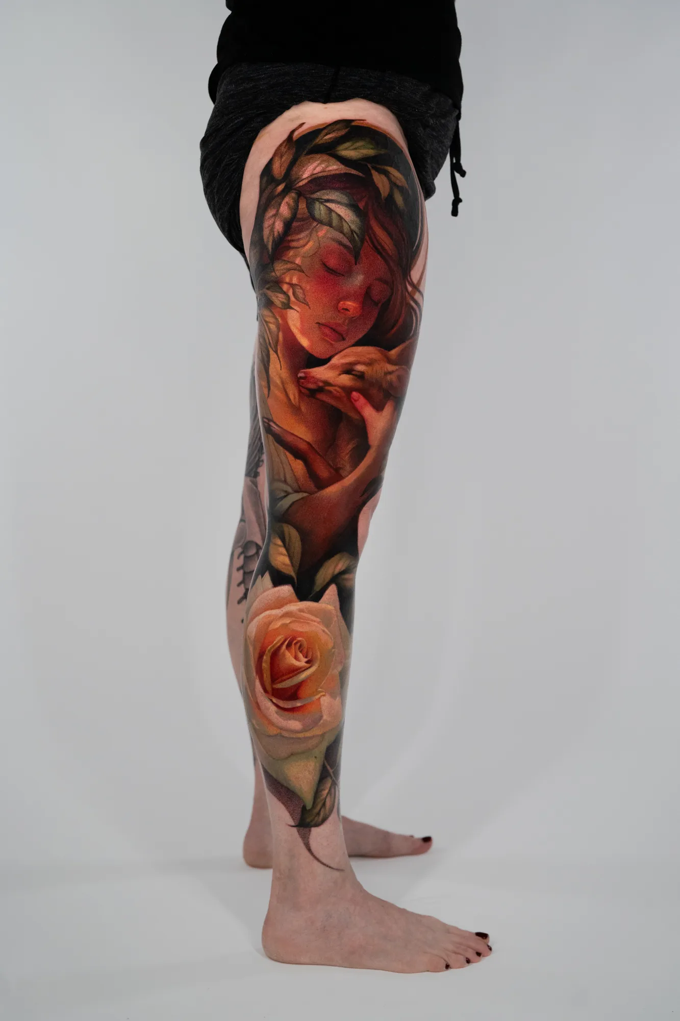 Full leg tattoo of a female figure caressing a deer and a yellow rose. 
