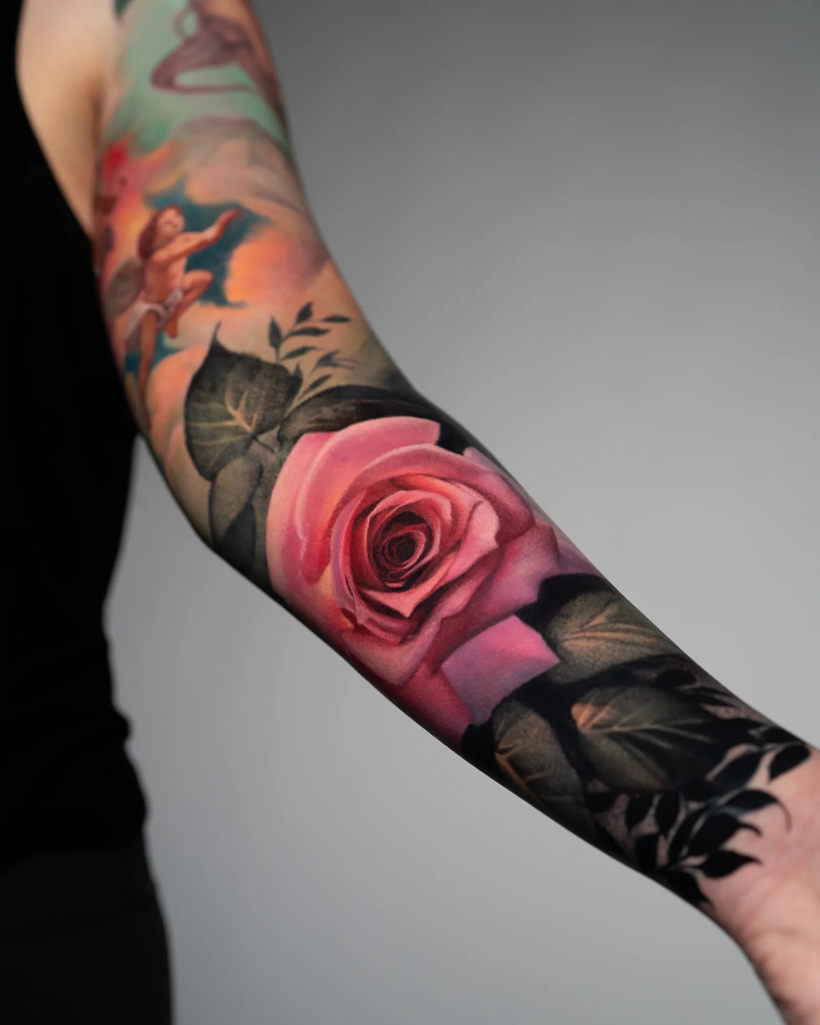 Painterly tattoo of a realistic pink rose on the forearm set on a dark background.