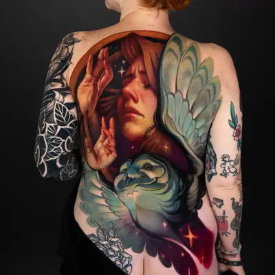 A colorful, painterly tattoo of a woman and an owl on the back.