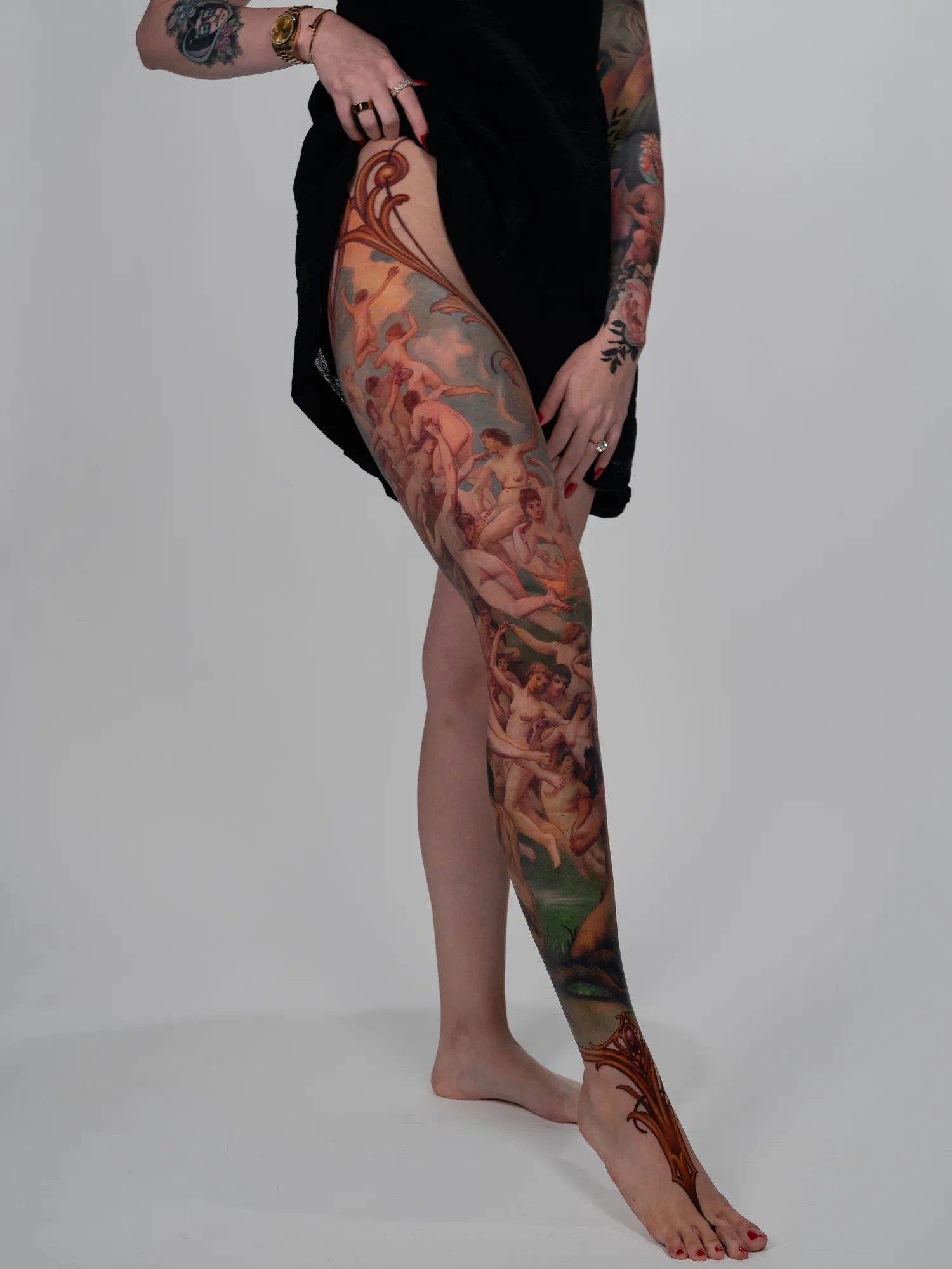 A detailed tattoo covering the leg with classical figures and ornamental designs.