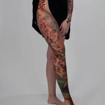 A detailed tattoo covering the leg with classical figures and ornamental designs.
