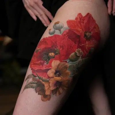 Vibrant floral tattoo featuring red poppies and orange blossoms on the thigh.