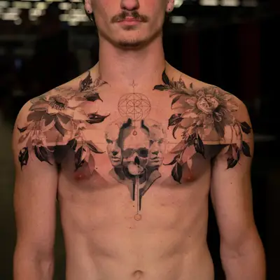Black and grey chest tattoo with a passionflower across each shoulder, a skull flanked by two classical faces at the center, and fine line geometric work above it.