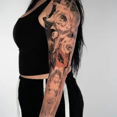 Black and grey realism full sleeve with large roses on the upper arm, a sword blade running down through them, and a draped classical statue on the forearm.