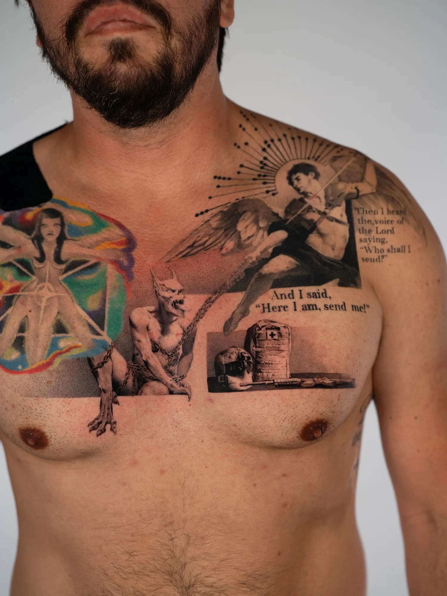 Black and grey chest tattoo of Saint Michael with a spear and a radiating dotwork starburst, a chained demon below, a military medic's helmet and aid bag, and scripture lettering from Isaiah.