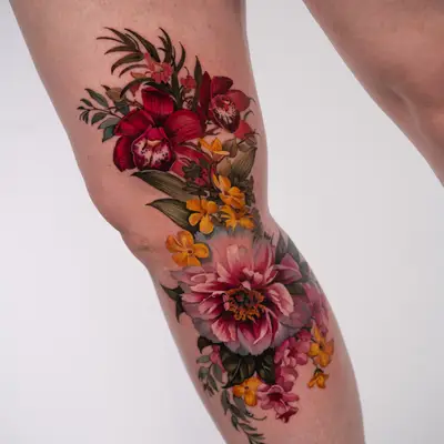 Full color realism tattoo of deep red orchids, yellow and orange flowers and a large pink peony running down the inside of a leg across the knee.