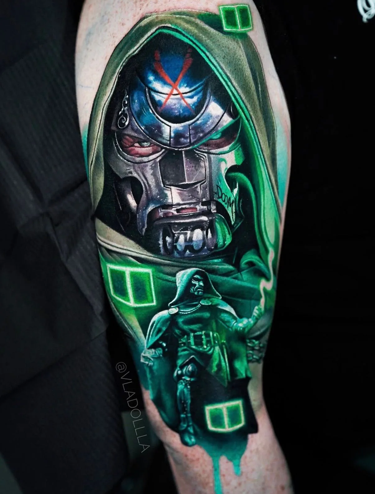 Tattoo of a metallic mask with green accents and a figure in a hooded cloak.