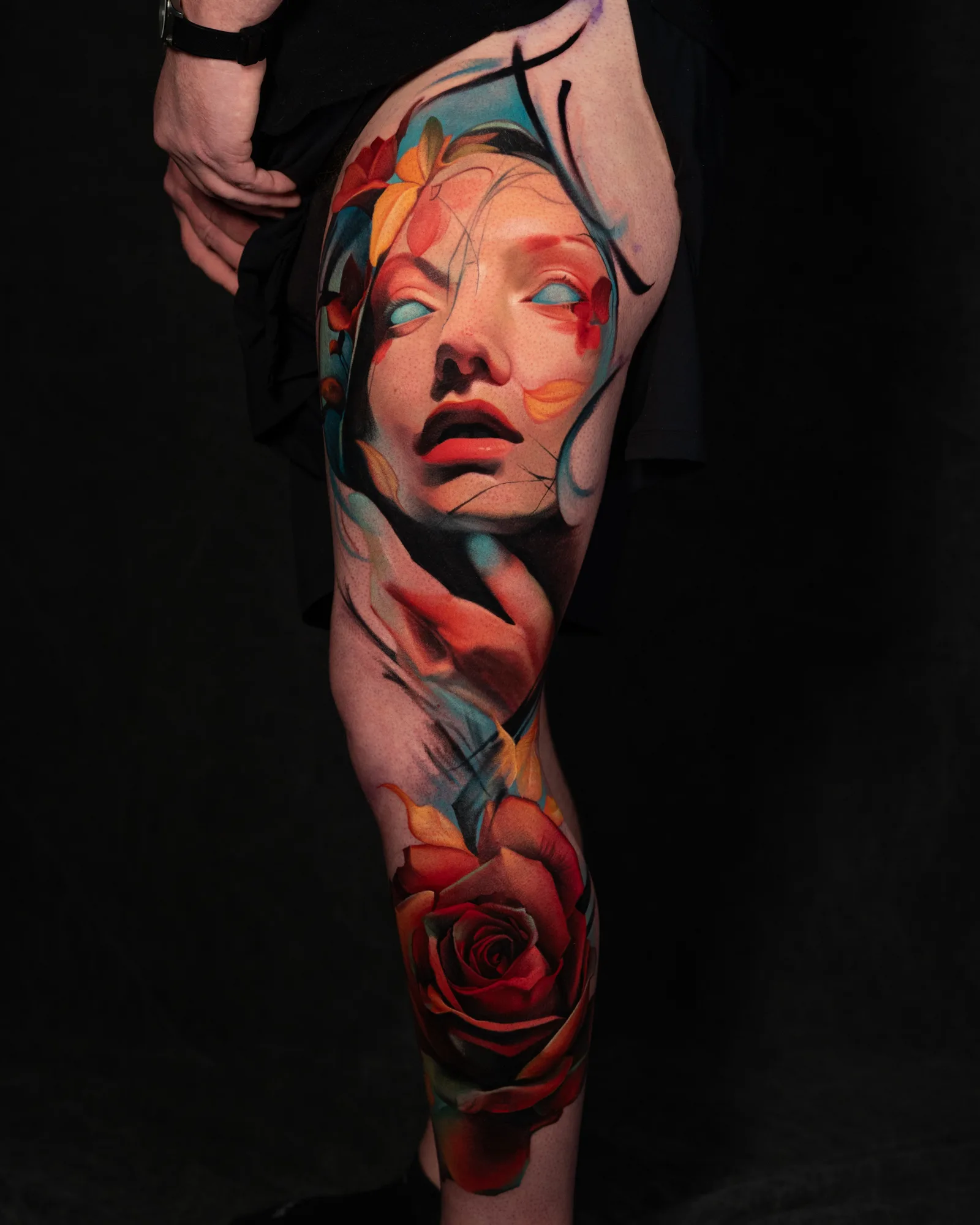 Colorful tattoo of a woman's face with flowers and a rose on leg