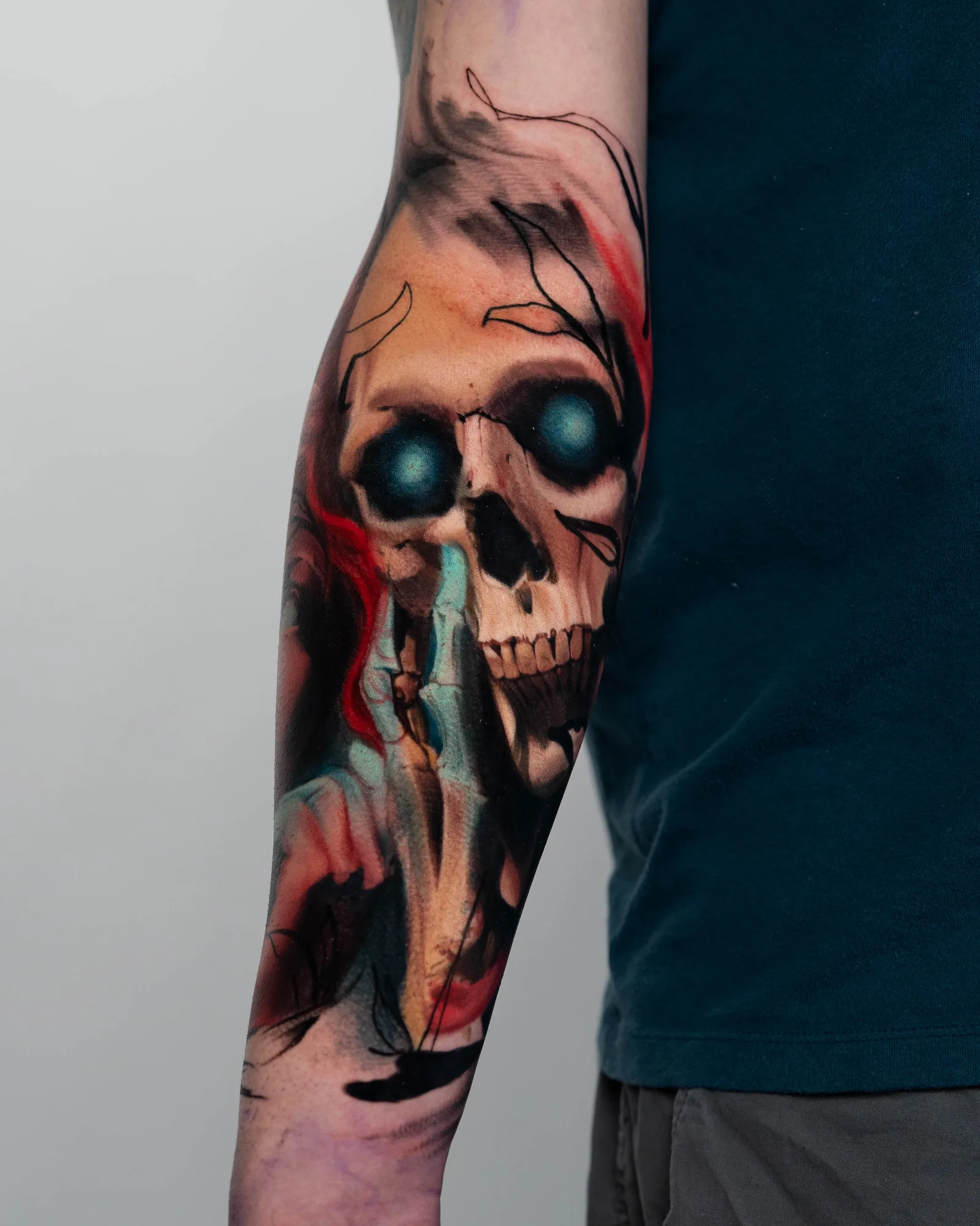 Tattoo of a skull with blue eyes and abstract elements on an arm.