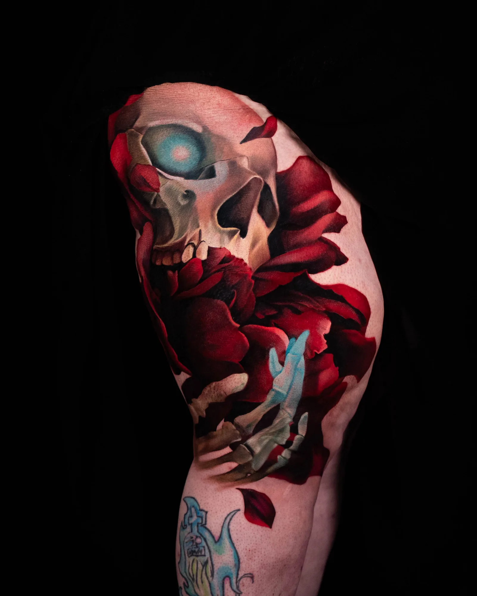 Tattoo of a skull with glowing eyes and red roses on an arm.