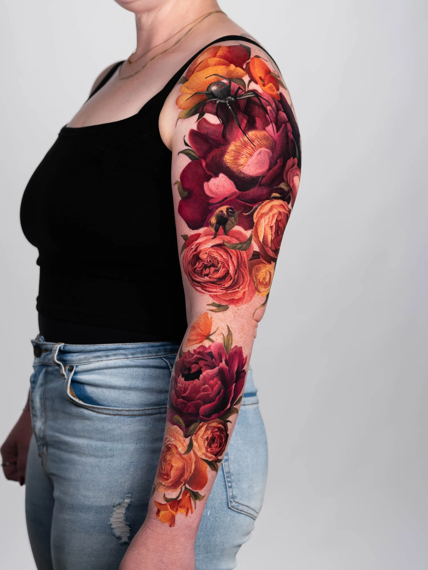 Floral sleeve tattoo with vibrant roses and a spider