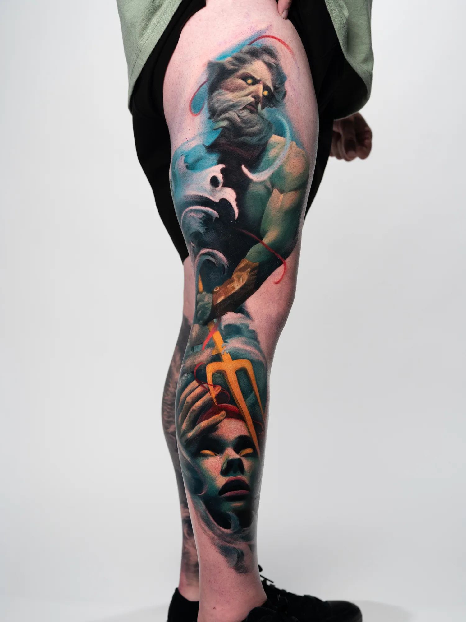 Colorful mythological tattoo on leg depicting a god and trident.