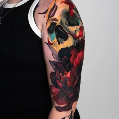 Tattoo of a skull with red flowers on upper arm.