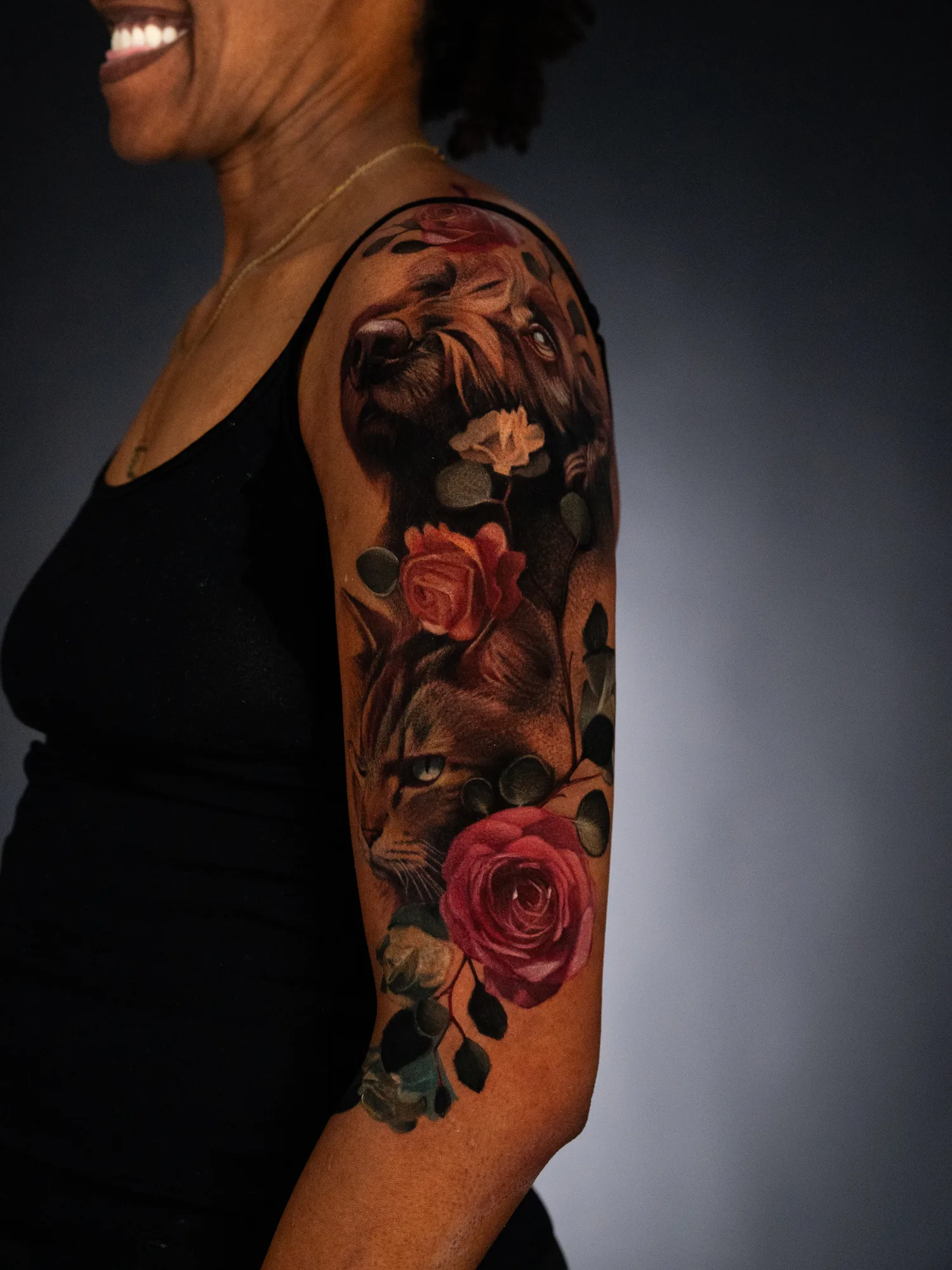Realistic tattoo of a dog and cat with roses on an upper arm.