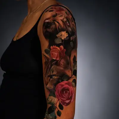 Realistic tattoo of a dog and cat with roses on an upper arm.