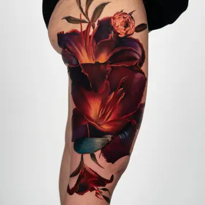 Tattoo of large lilies in a fiery color palette on a woman's thigh.