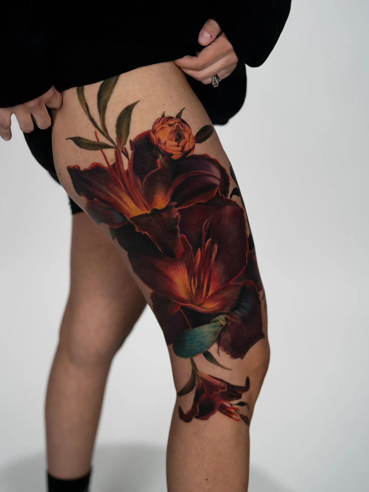 Tattoo of large lilies in a fiery color palette on a woman's thigh.