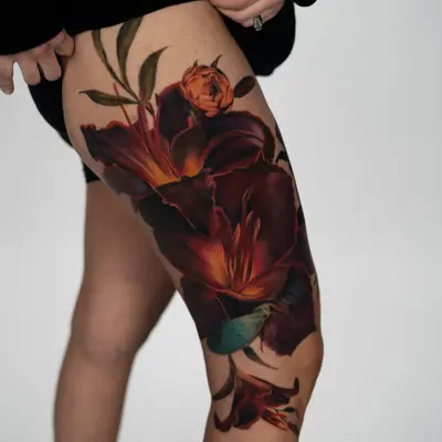 Tattoo of large lilies in a fiery color palette on a woman's thigh.