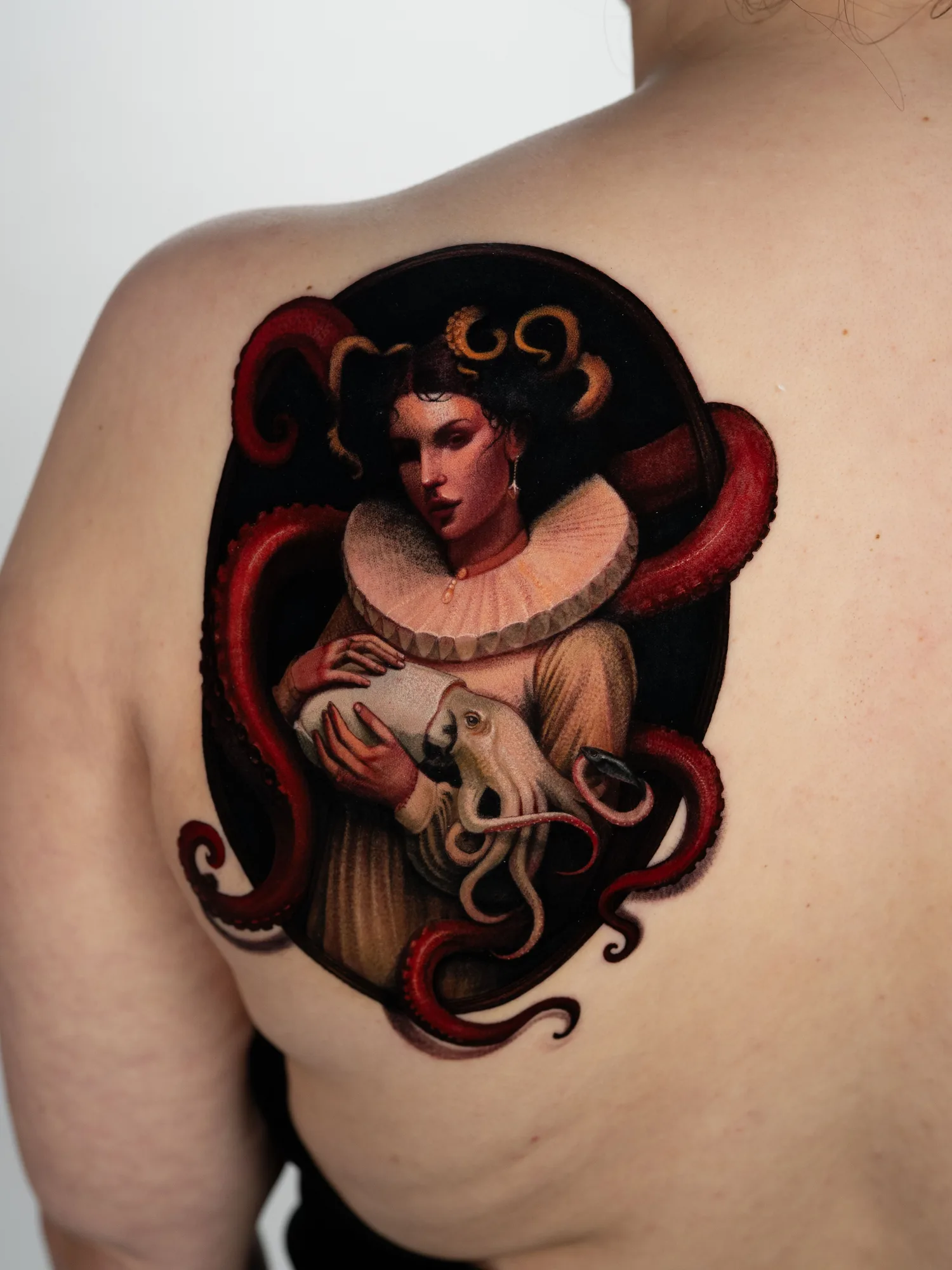 A painterly tattoo of a woman holding an octopus, with red tentacles wrapped around her.