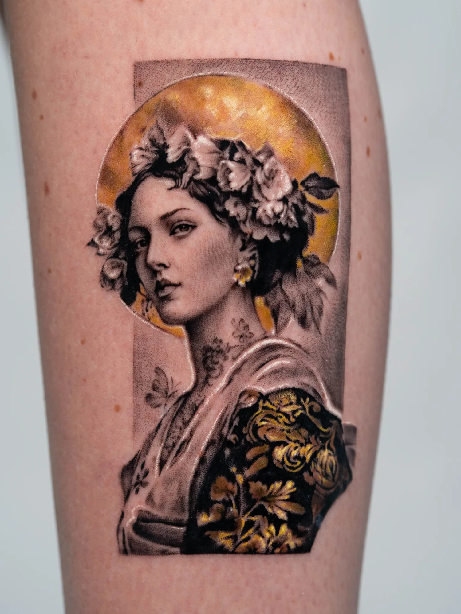 Tattoo of a female portrait in black and grey set on a gold leaf circle.