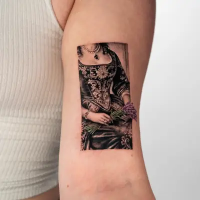 Micorealism tattoo in black and grey of a woman in a Victorian dress holding wisteria flowers in color.