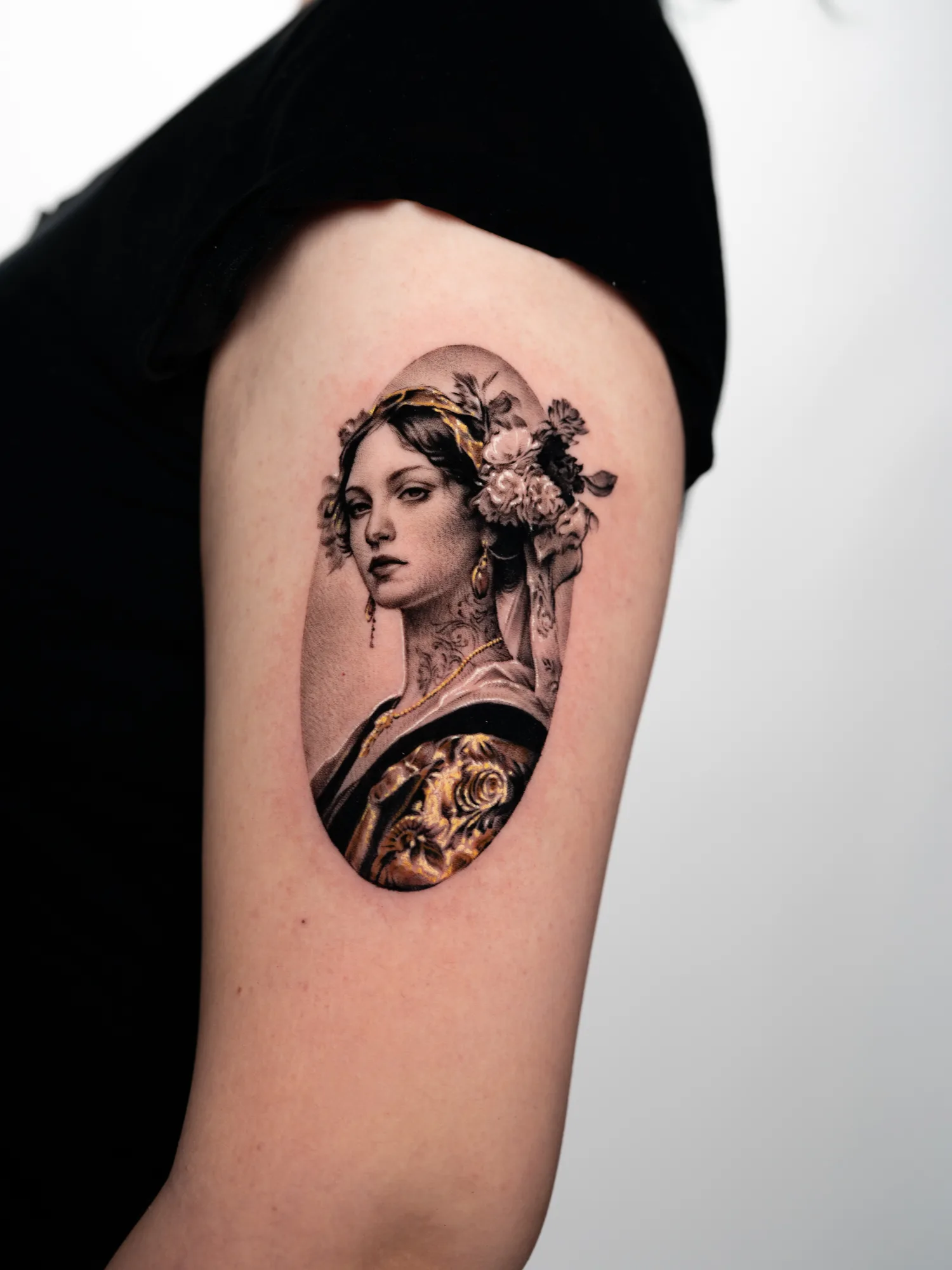 Black and grey tattoo of a woman with flowers in her hair and gold accents.