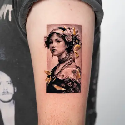 Black and grey tattoo of a woman with flowers in her hair and gold accents.