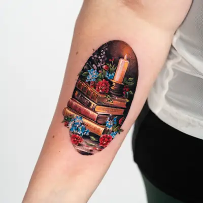 Tattoo of a still life with books, a candle, and flowers on an inner forearm