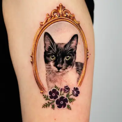 Tattoo of a cat in a gold frame with flowers on an upper arm.
