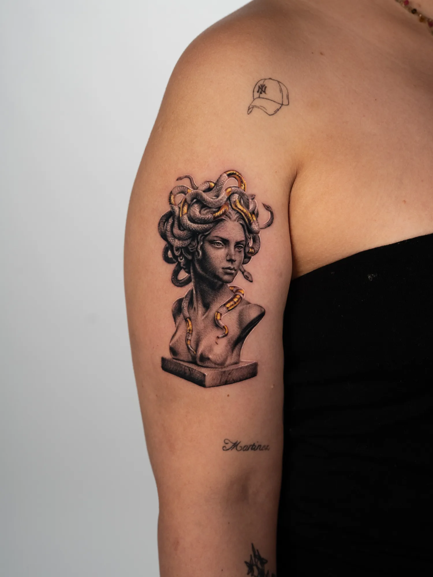 Tattoo of a bust of Medusa on an upper forearm in black and grey with gold snakes.