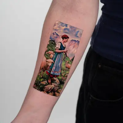 Color painterly tattoo of a shepherdess in a dirndl standing among sheep in an alpine meadow with snow-capped mountains behind, on a forearm.