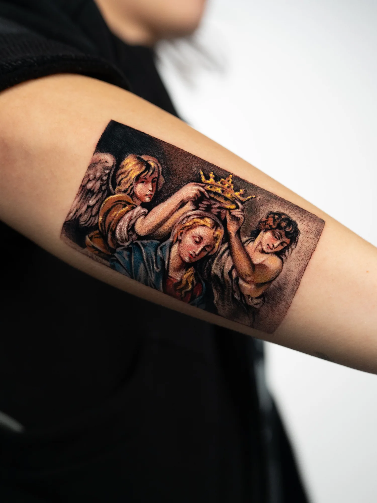 Color painterly tattoo of two angels lowering a gold crown onto the head of the Virgin, after a Baroque painting, on a forearm.