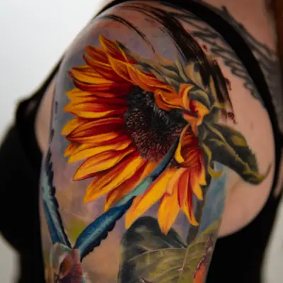 Tattoo of a sunflower with a bird and butterfly on upper arm.