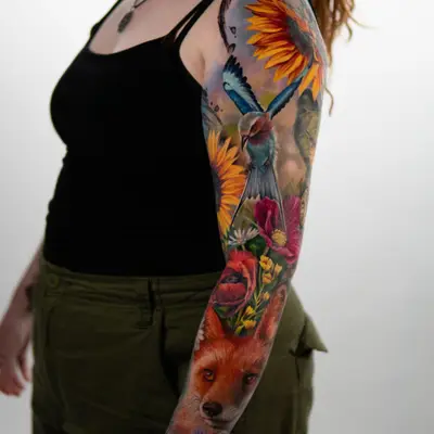 Colorful sleeve tattoo featuring a fox, flowers, and a bird.