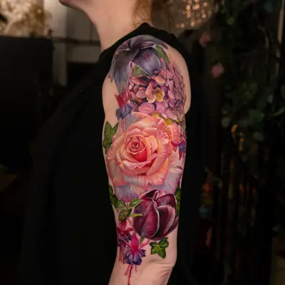 Colorful floral tattoo on upper arm featuring roses and lilies.
